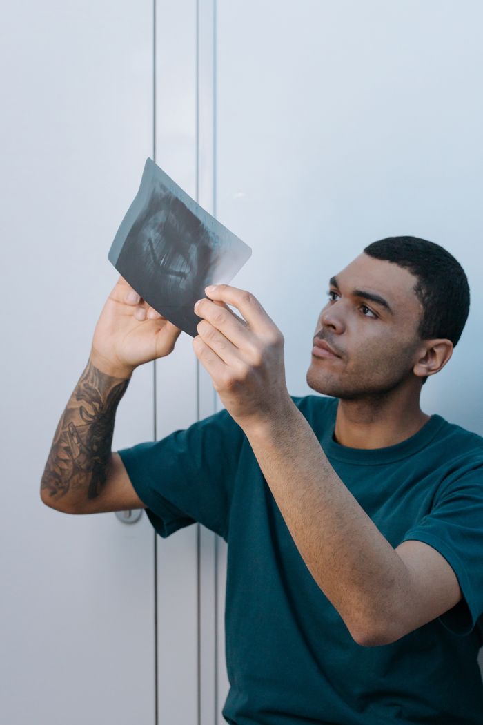 A focused young adult male closely examines a dental X-ray in a clinic environment.