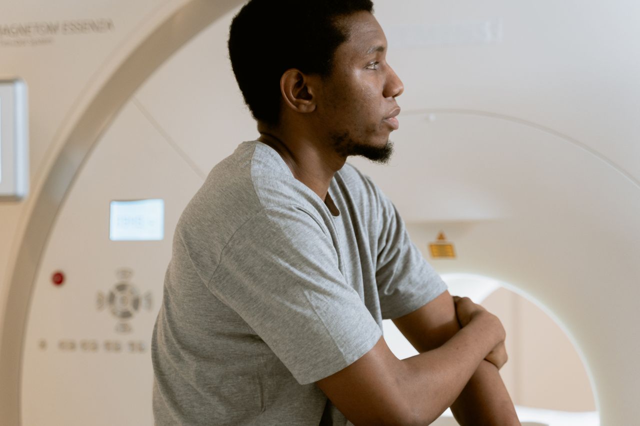 A man sits before a CT scanner, preparing for a medical examination, conveying a sense of anticipation.